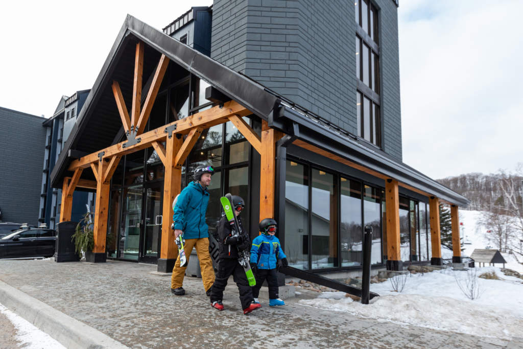 Father and two sons leaving the condo walking with skis towards the ski hill