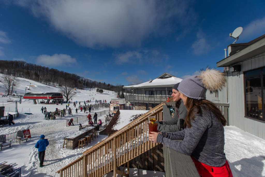 Two women in base layers and snowpants on the apres patio having a drink